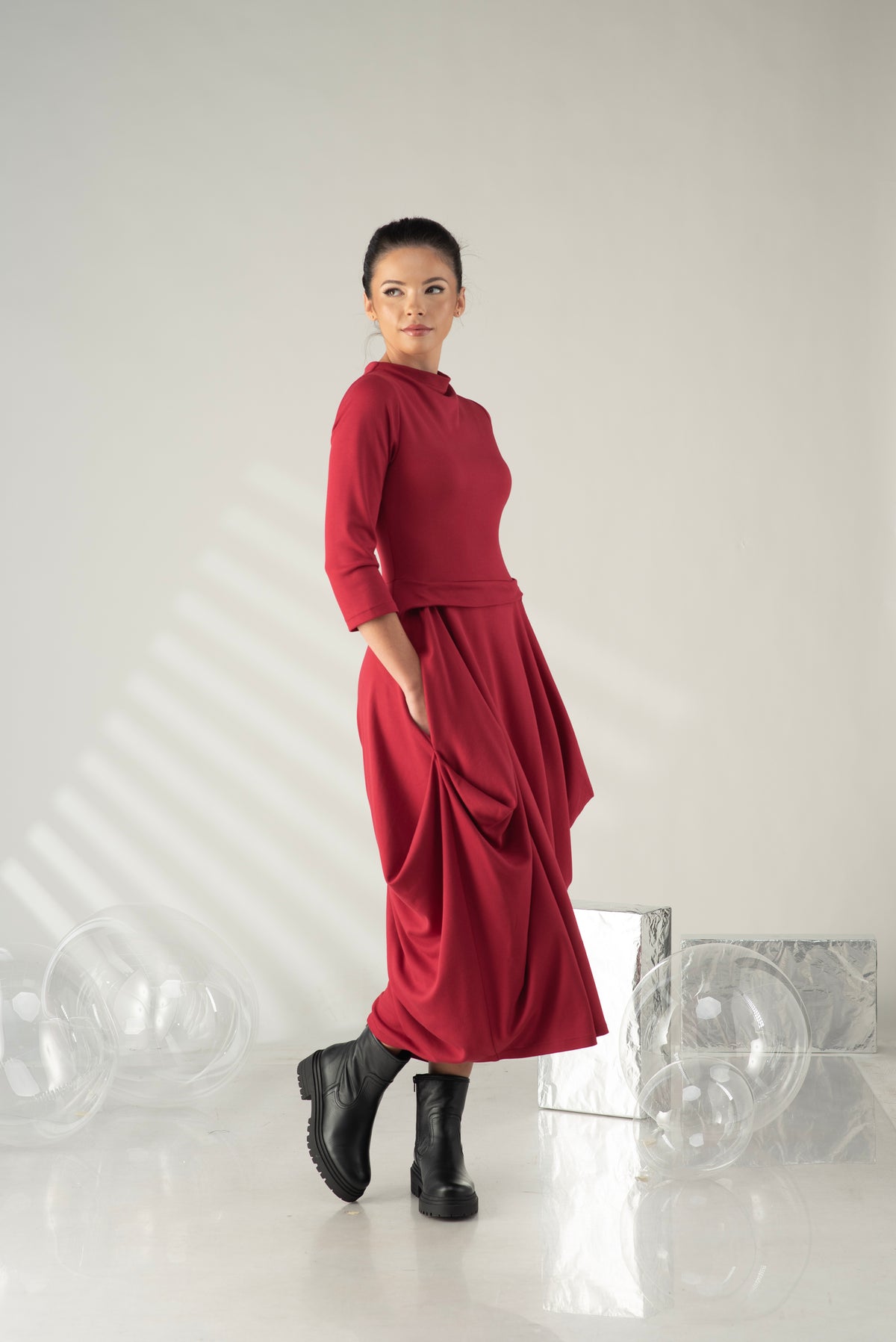 Woman wearing a red dress and black boots standing against a white background