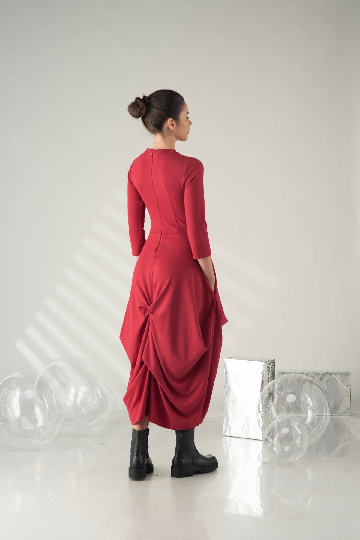Woman wearing a red dress standing in a minimalistic room with white walls and floor.