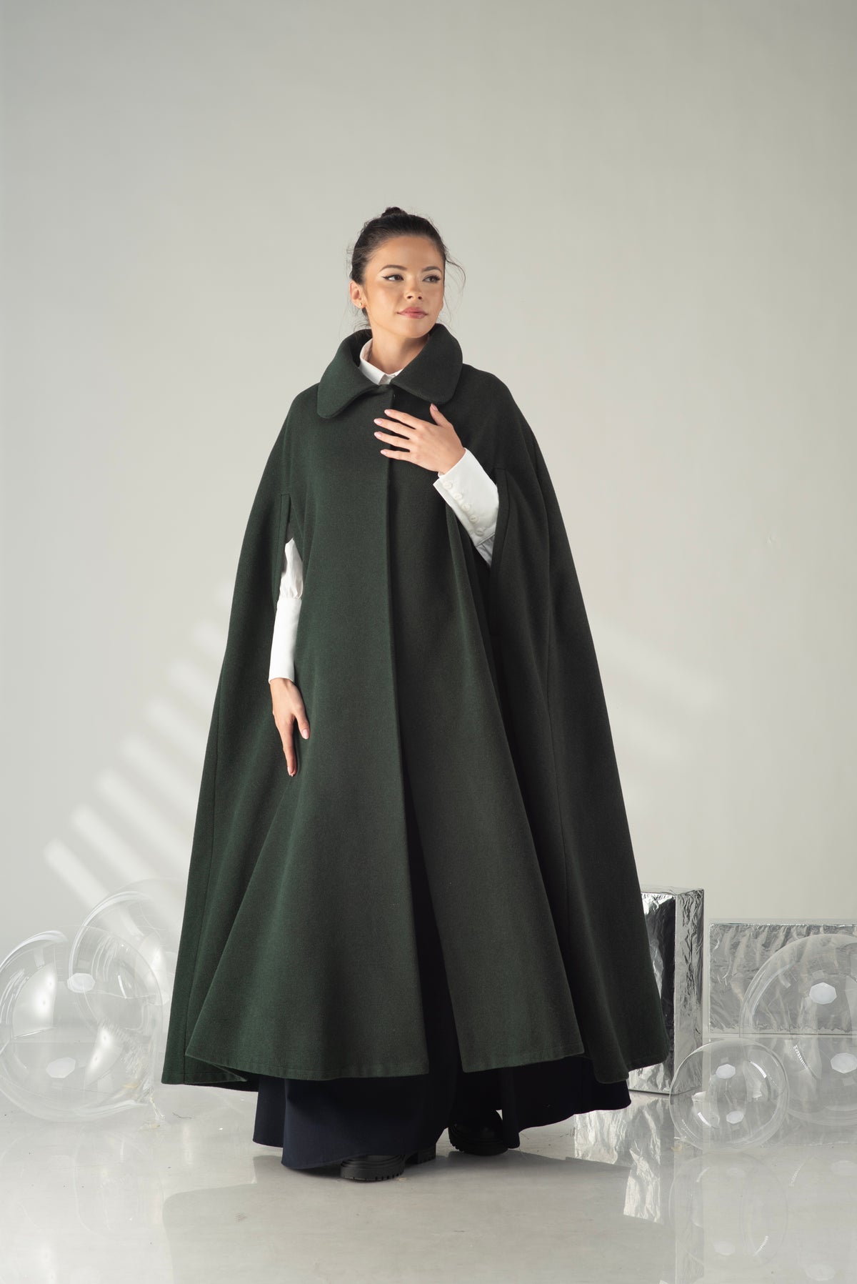 Women's dark green hooded cape coat styled over a long dress