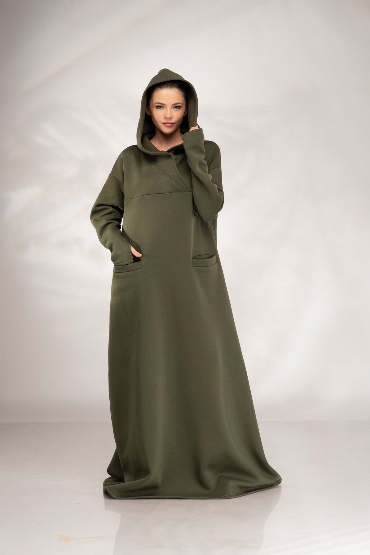 Women’s olive green hooded maxi sweatshirt dress, front view with hood up and hand in front pocket